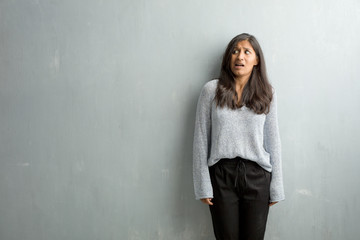 Young indian woman against a grunge wall very scared and afraid, desperate for something, cries of...