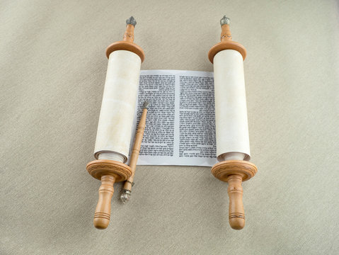 The unfolded scroll of the Torah and the pointer lies on the rough canvas.