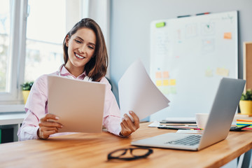 Smiling young woman looking at business documents working in home office - obrazy, fototapety, plakaty