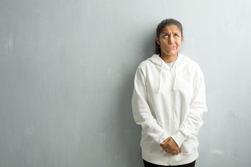 Young sporty indian woman against a gym wall doubting and confused, thinking of an idea or worried about something