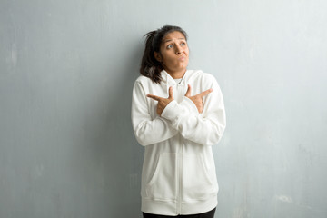 Young sporty indian woman against a gym wall confused and doubtful man, decide between two options, concept of indecision