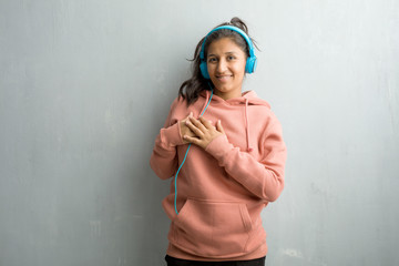 Young sporty indian woman against a wall doing a romantic gesture, in love with someone or showing affection for some friend. Listening music with headphones.
