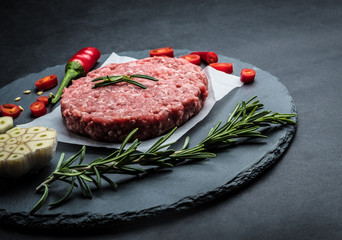 Raw ground beef meat burger steak cutlet with chili, rosemary and garlic on black slate plate for cooking