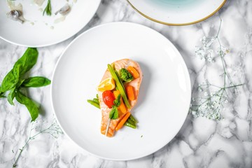 steamed salmon steak with vegetables on a white marble table