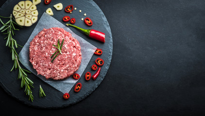 Raw burger cutlet from beef meat with garlic and rosemary on black background with copy space, top view