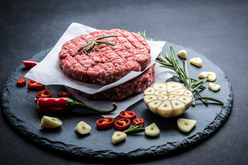 Raw ground beef meat burger steak cutlet with chili, rosemary and garlic on black slate plate for cooking