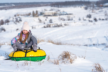 Young little girl laughing and enjoying snow tubing on the snowy hill at winter