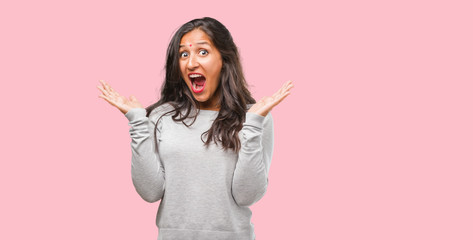 Portrait of young indian woman screaming happy, surprised by an offer or a promotion, gaping, jumping and proud