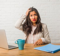 Young indian woman at the office worried and overwhelmed, forgetful, realize something, expression...