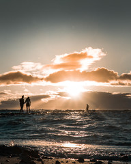 A couple of people goes into the ocean towards a person during sunset
