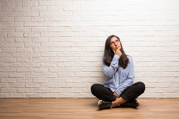 Young indian woman sit against a brick wall doubting and confused, thinking of an idea or worried about something