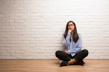 Young indian woman sit against a brick wall doubting and confused, thinking of an idea or worried...