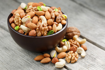 Wooden bowl with mixed nuts on a wooden gray background. Walnut, pistachios, almonds, hazelnuts and...
