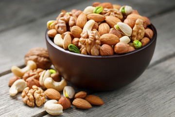 Obraz na płótnie Canvas Wooden bowl with mixed nuts on a wooden gray background. Walnut, pistachios, almonds, hazelnuts and cashews, walnut.