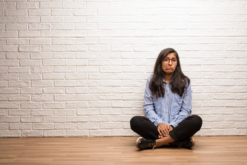 Young indian woman sit against a brick wall worried and overwhelmed, forgetful, realize something,...