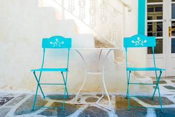 Beautilul turquoise chairs and white table on the background of white building on greek street