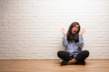 Young indian woman sit against a brick wall crazy and desperate, screaming out of control, funny lunatic expressing freedom and wild