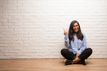Young indian woman sit against a brick wall fun and happy, positive and natural, doing a gesture of victory, peace concept