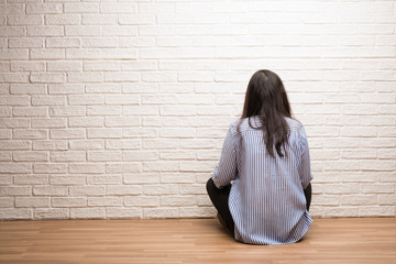 Young indian woman sit against a brick wall showing back, posing and waiting, looking back