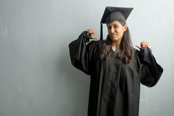 Young graduated indian woman against a wall proud and confident, pointing fingers, example to follow, concept of satisfaction, arrogance and health