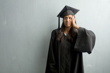 Young graduated indian woman against a wall worried and overwhelmed, forgetful, realize something, expression of shock at having made a mistake