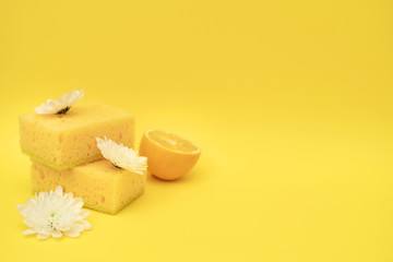 Pile of yellow polyurethane sponges laying near lemon and white flowers