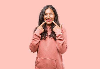 Portrait of fitness young indian woman smiles, pointing mouth, concept of perfect teeth, white teeth, has a cheerful and jovial attitude