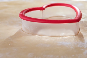 Close up view of a red heart cookie cutter on a sheet of sugar cookie dough sprinkled with flour. ...