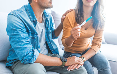 Cropped shot of depressed couple sitting and holding pregnancy test