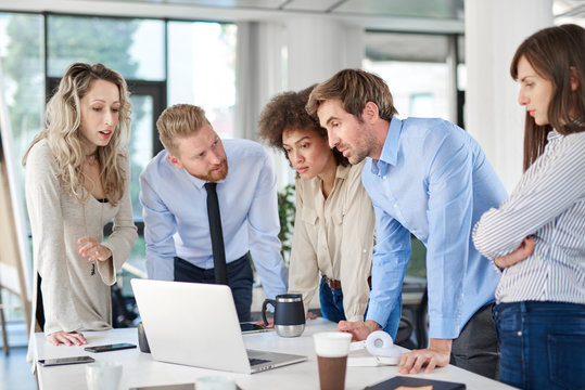 Small Group Of Business People Standing In Office, Looking At Laptop And Developing Business Plan. Start Up Business Concept.