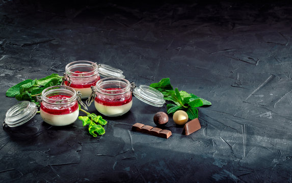 Panna cotta with strawberry jam. Sweet italian dessert from whipped cream with strawberry jam in glass jars. Dark background
