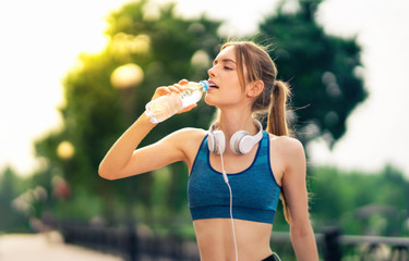 Woman in sportswear drinking water, during morning jogging or workout, outdoors