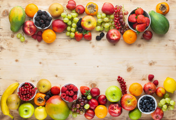 Healthy fruits berries background, strawberries raspberries oranges plums apples kiwis grapes blueberries mango persimmon on the wooden table, top view, copy space for text, selective focus