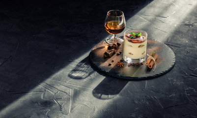 Sweet tiramisu in glass with a glass of cognac on dark background