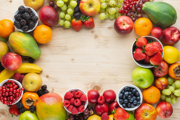 Rainbow fruits background frame, strawberries raspberries oranges plums apples kiwis grapes blueberries mango persimmon on light wooden table, top view, copy space for text, selective focus - obrazy, fototapety, plakaty