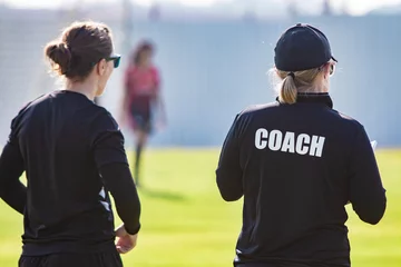 Foto op Plexiglas Back view of female sport coach and her assistant in black COACH shirt at an outdoor sport field © kudosstudio