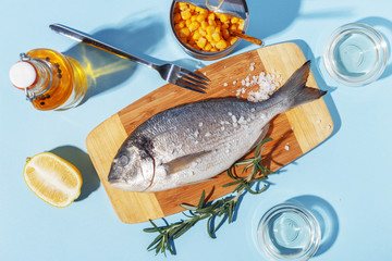 Raw dorado fish on a wooden board, ingredients for cooking and spices on a blue background.