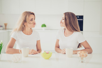 Close up photo two people mum teen daughter pretending man male guy making moustache hair funky face expression fooling around beverage sweets on table wear white t-shirts jeans bright flat kitchen
