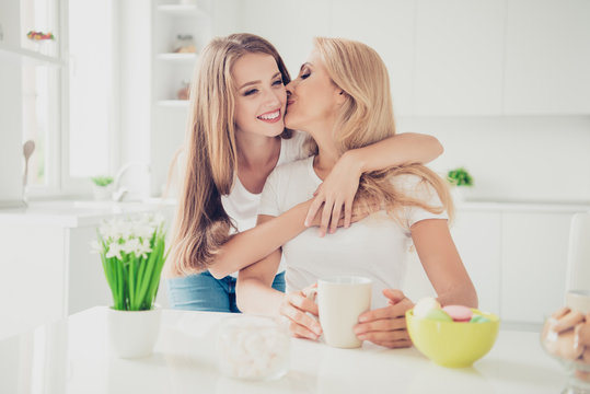 Close Up Photo Piggy-back Two People Mum And Teen Daughter Drink Tea Coffee Family Moment Lovely Lean On Mommy Woman Holiday Kiss Cheek Wear White T-shirts Jeans In Bright Flat Kitchen