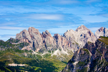 Rocky dolomitic mountains and green valley on a summer day with some clouds, during a tourist walk