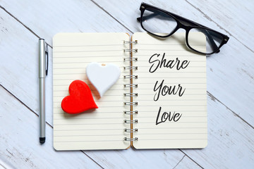 Top view of glasses,wooden heart,pen and notebook written with Share Your Love. Advice and motivation.