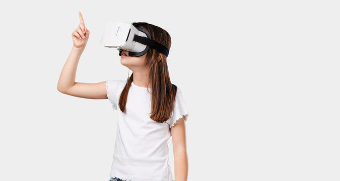 Full body little girl excited and entertained, playing with virtual reality glasses, exploring a fantasy world, trying to touch something