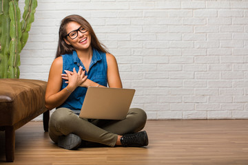 Portrait of young latin woman sitting on the floor doing a romantic gesture, in love with someone or showing affection for some friend. Holding a laptop.