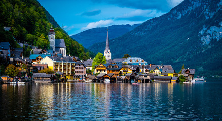 Sunshine evening scenery of beautiful Hallstatt at the wide lake on the background of rocky forested mountains