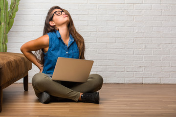 Portrait of young latin woman sitting on the floor with back pain due to work stress, tired and...