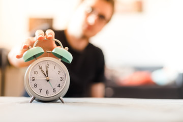Man is pushing an alarm clock in the morning, sunshine and blurry background