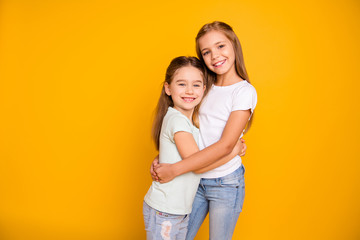 Portrait of two nice-looking cute winsome sweet attractive lovely pretty cheerful cheery positive caucasian straight-haired girls cuddling isolated over bright vivid shine yellow background