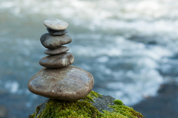 Fototapeta na wymiar Closeup of stone balance on rock covered by moss in border river