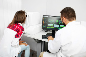 Teenage girl udergoes eye survey with doctor on tomograph in ophthalmologic clinic