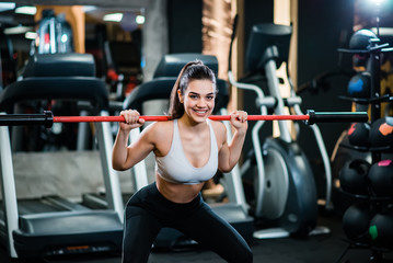 Portrait of athletic girl doing squats with a bar in the gym, smiling at camera.